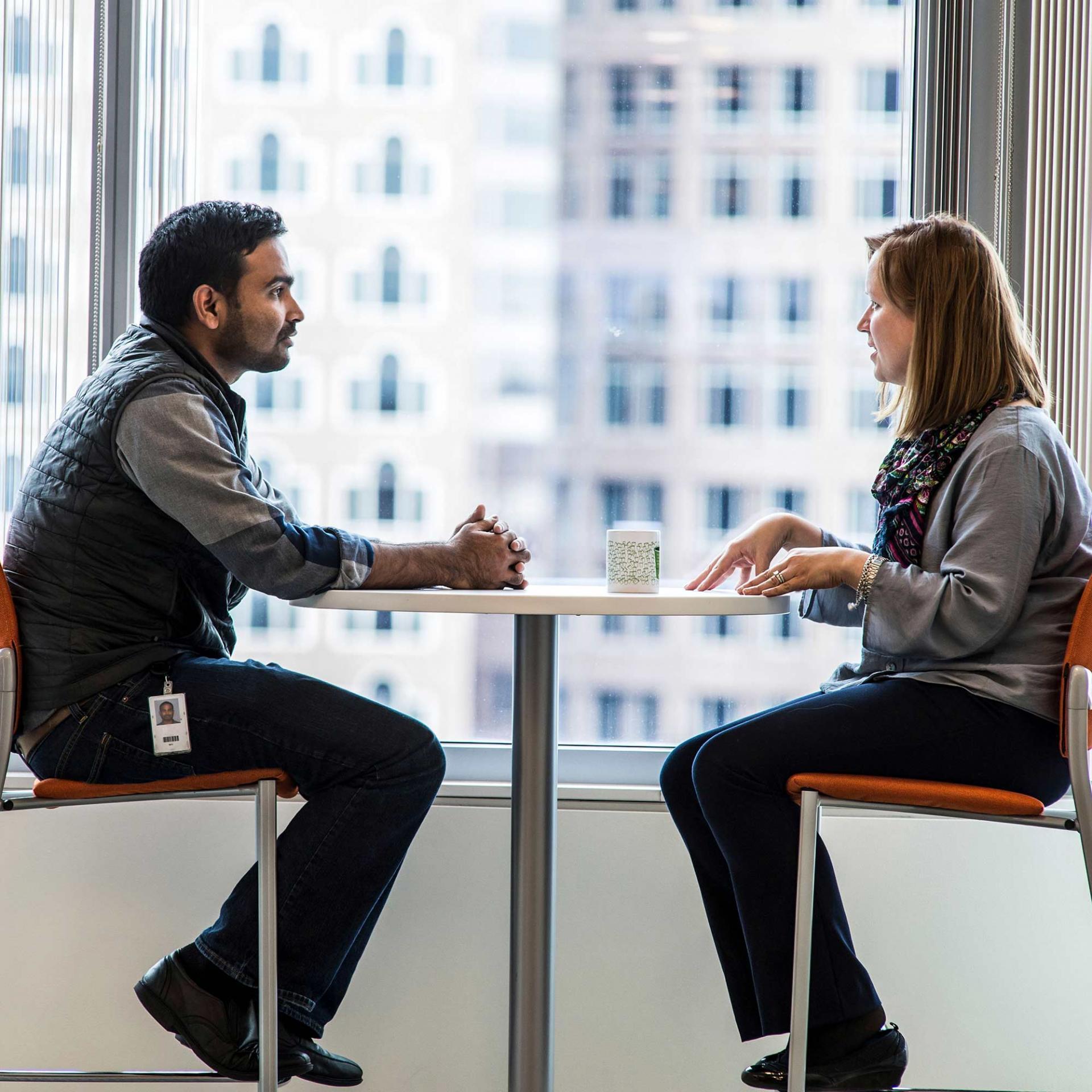 Two Vertex employees sitting by a window having a discussion