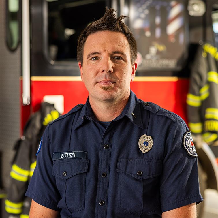 An image of Cody Burton looking at the camera with a serious look on his face while standing in front of a firetruck.