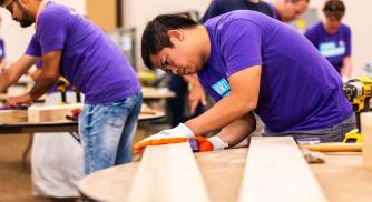 An image of a Vertex Pharmaceuticals employee wearing a purple shirt while working on a plank of wood during Vertex's 16th Annual Global Week of Service