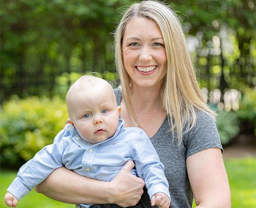 An image of Maighan smiling at the camera while holding her baby.