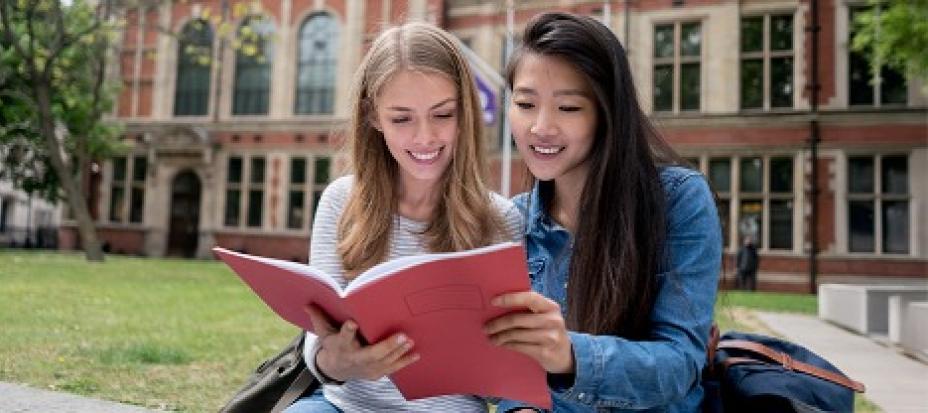 Two girls sitting outside together reading a book