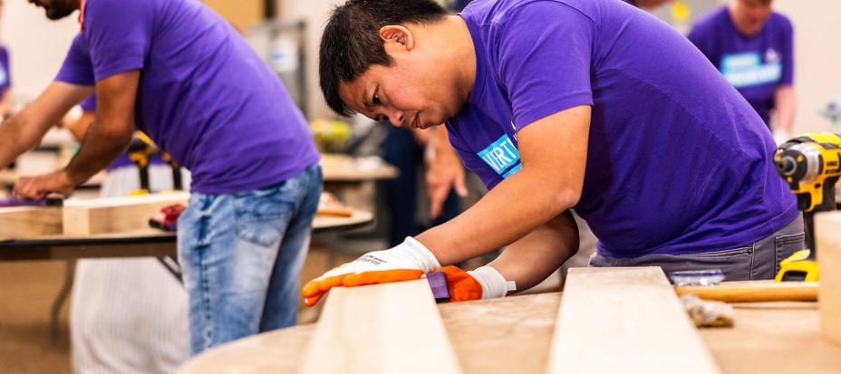An image of a Vertex Pharmaceuticals employee wearing a purple shirt while working on a plank of wood during Vertex's 16th Annual Global Week of Service