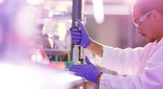 A Vertex scientist in a lab wearing a white coat and purple gloves while using lab equipment during an experiment