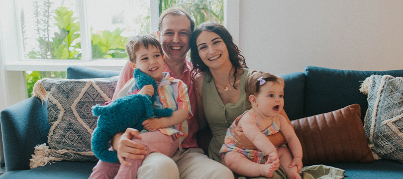 An image of a Victoria Newcomb and her partner sitting on a couch holding their two children