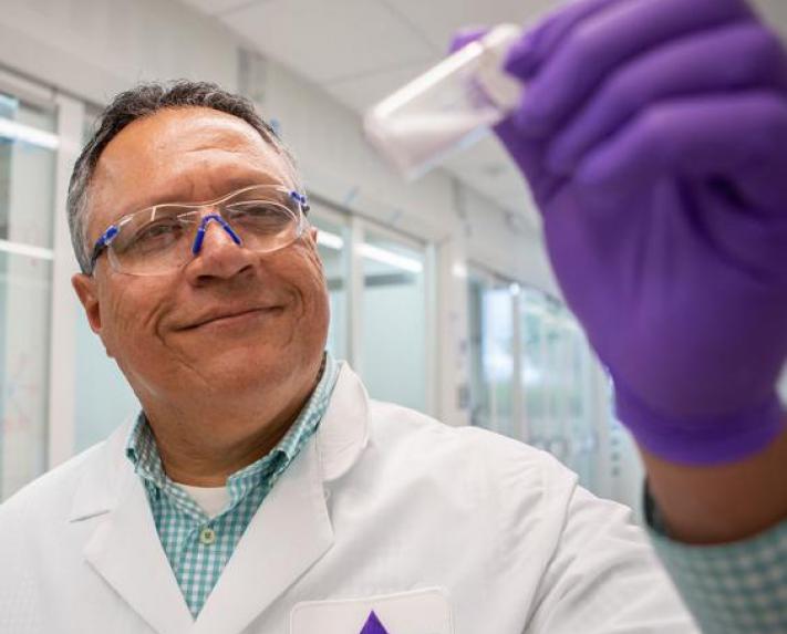 A Vertex scientist in a lab coat holds up a vial containing a white substance