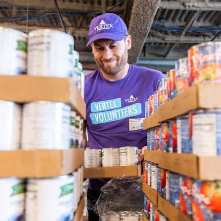 An image of a Vertexian wearing a purple shirt while volunteering at a local foodbank