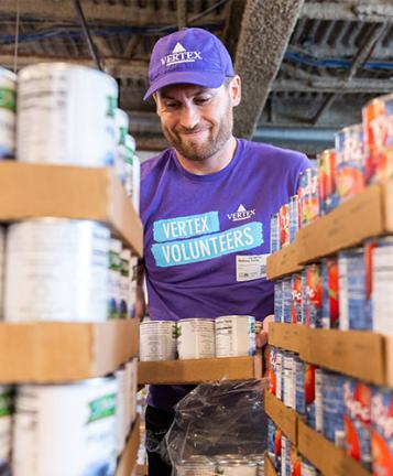 An image of a Vertexian wearing a purple shirt while volunteering at a local foodbank