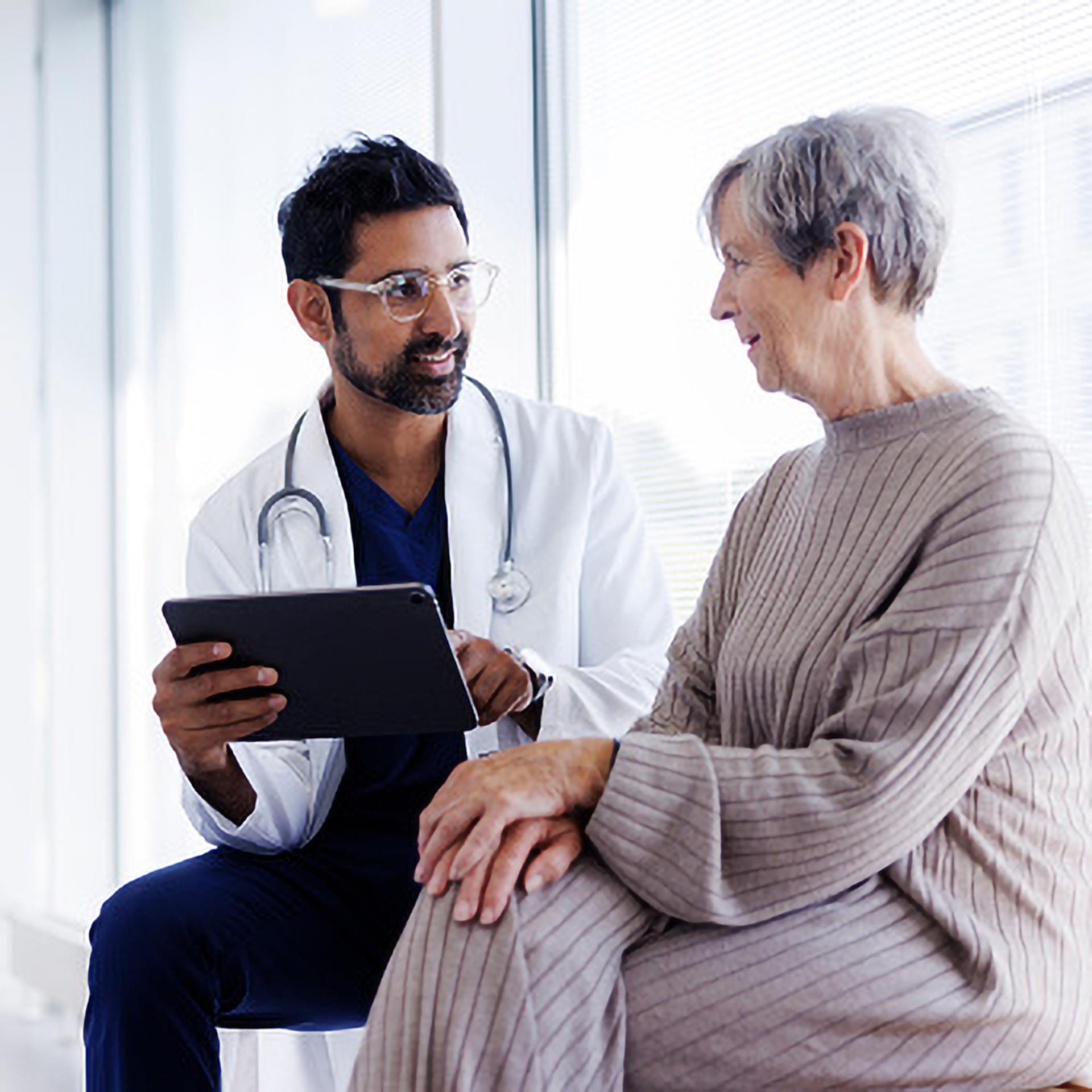 A doctor holding a tablet discussing something with an elderly patient