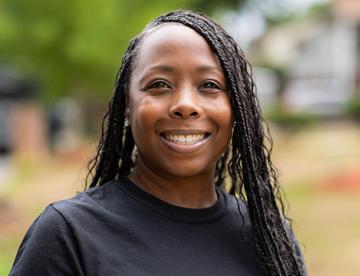 An image of Sharron Rouse wearing a black shirt standing outside smiling at the camera