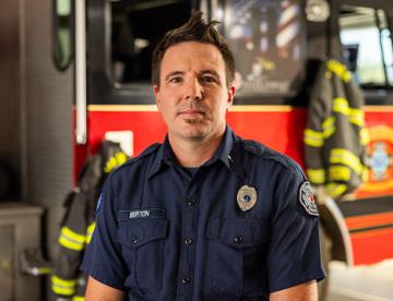 An image of Cody Burton standing in front of a firetruck wearing his firefighter uniform.