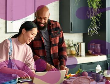 An image of a man and a woman in a kitchen looking at a computer screen while they cook food