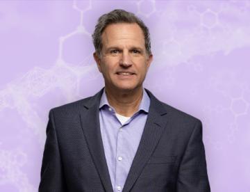An image of Paul Negulescu smiling while standing in front of a purple background that has faded diagrams of molecules in it