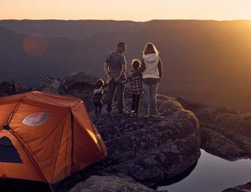 An image of a family of four standing on a cliff looking at a sunset