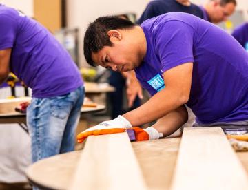 An image of a Vertex Pharmaceuticals employee wearing a purple shirt while working on a plank of wood during Vertex's 16th Annual Global Week of Service