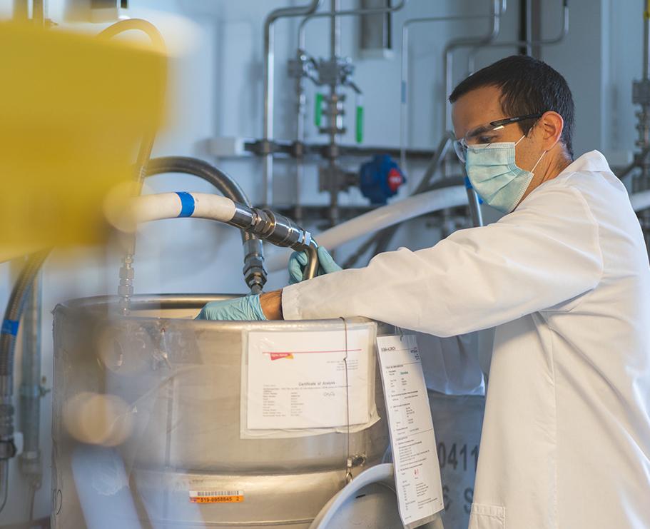 A scientist adjusting some equipment in a lab while wearing a mask