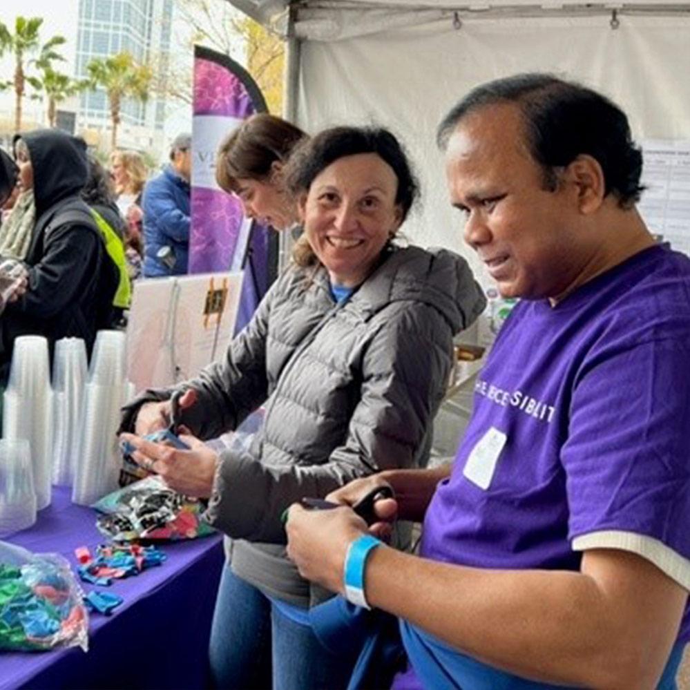 An image of two Vertex Pharmaceuticals employees (one female, one male) standing outside cutting balloons for a science experiment booth at the San Diego Festival of Science & Engineering.