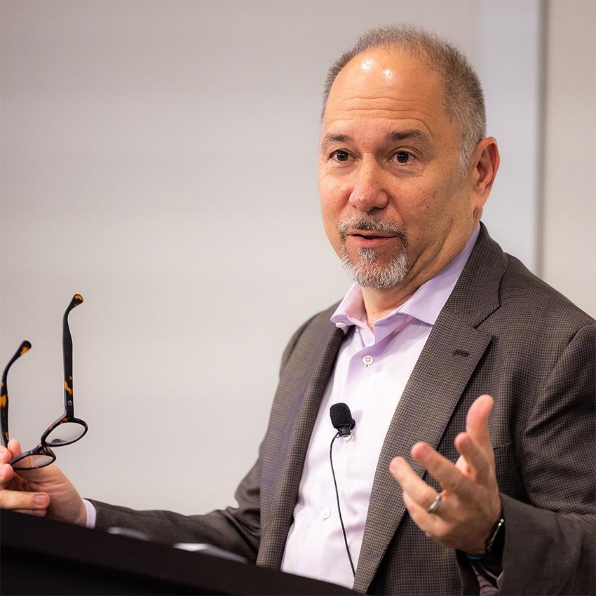 An image of David Altshuler, Executive Vice President and Chief Scientific Officer at Vertex Pharmaceuticals speaking at a podium with his glasses in his right hand