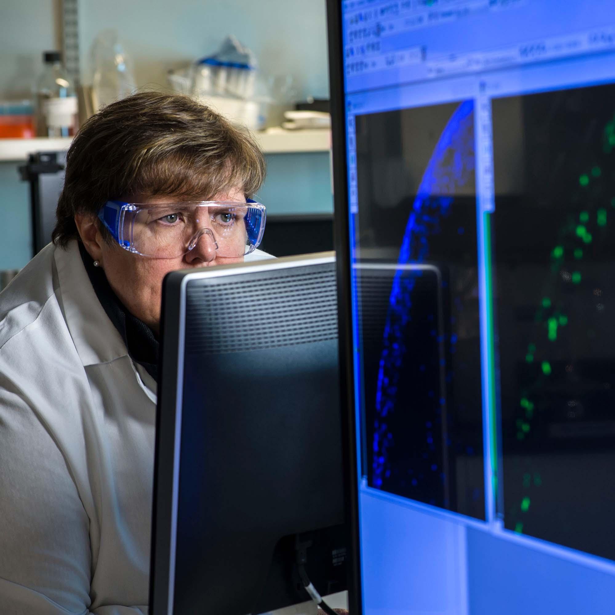 A female Vertex scientist wearing goggles studies a computer monitor