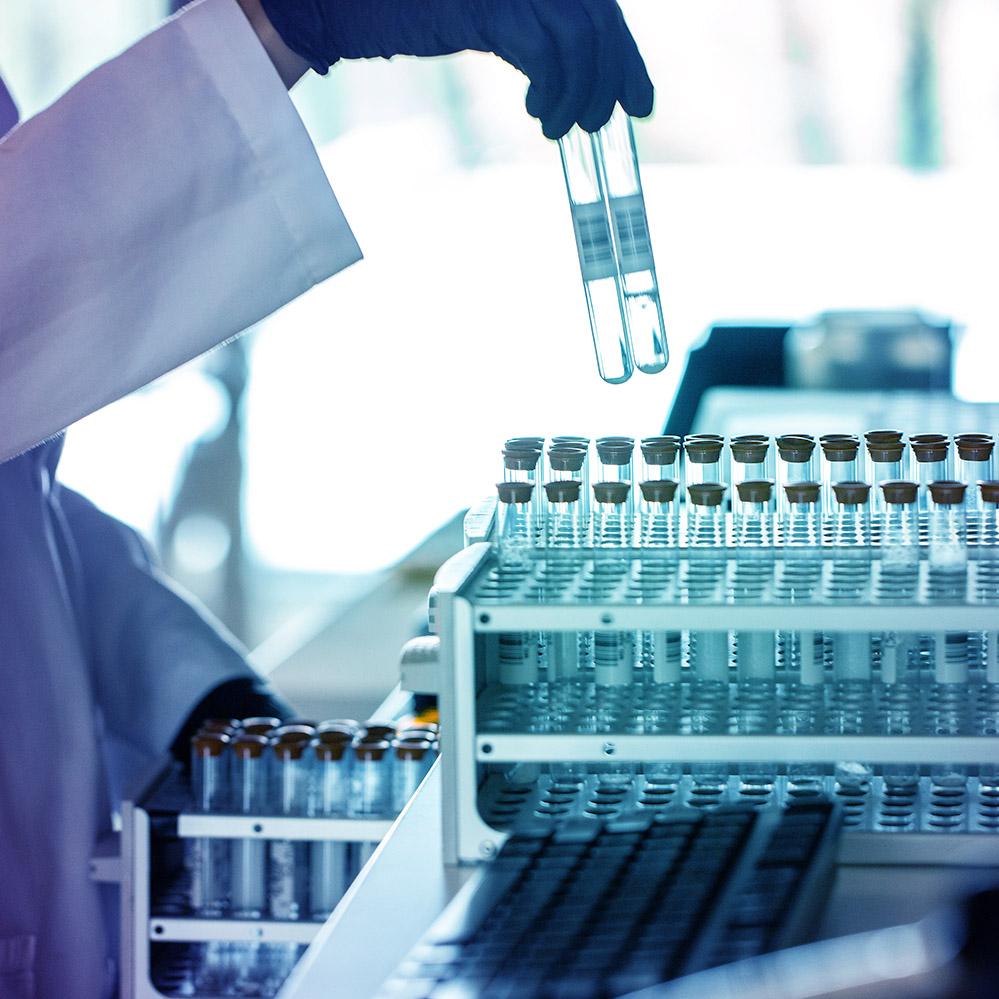 An image of a scientist's hand pulling two test tubes out of a rack