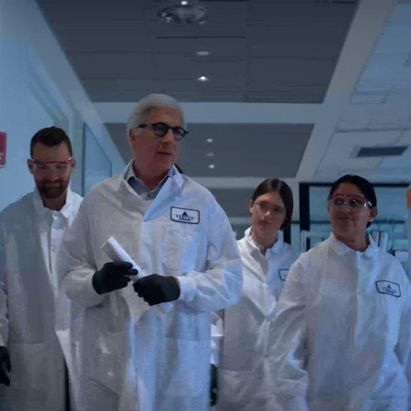 An image of 4 Vertex scientists wearing lab coats walking down a hallway