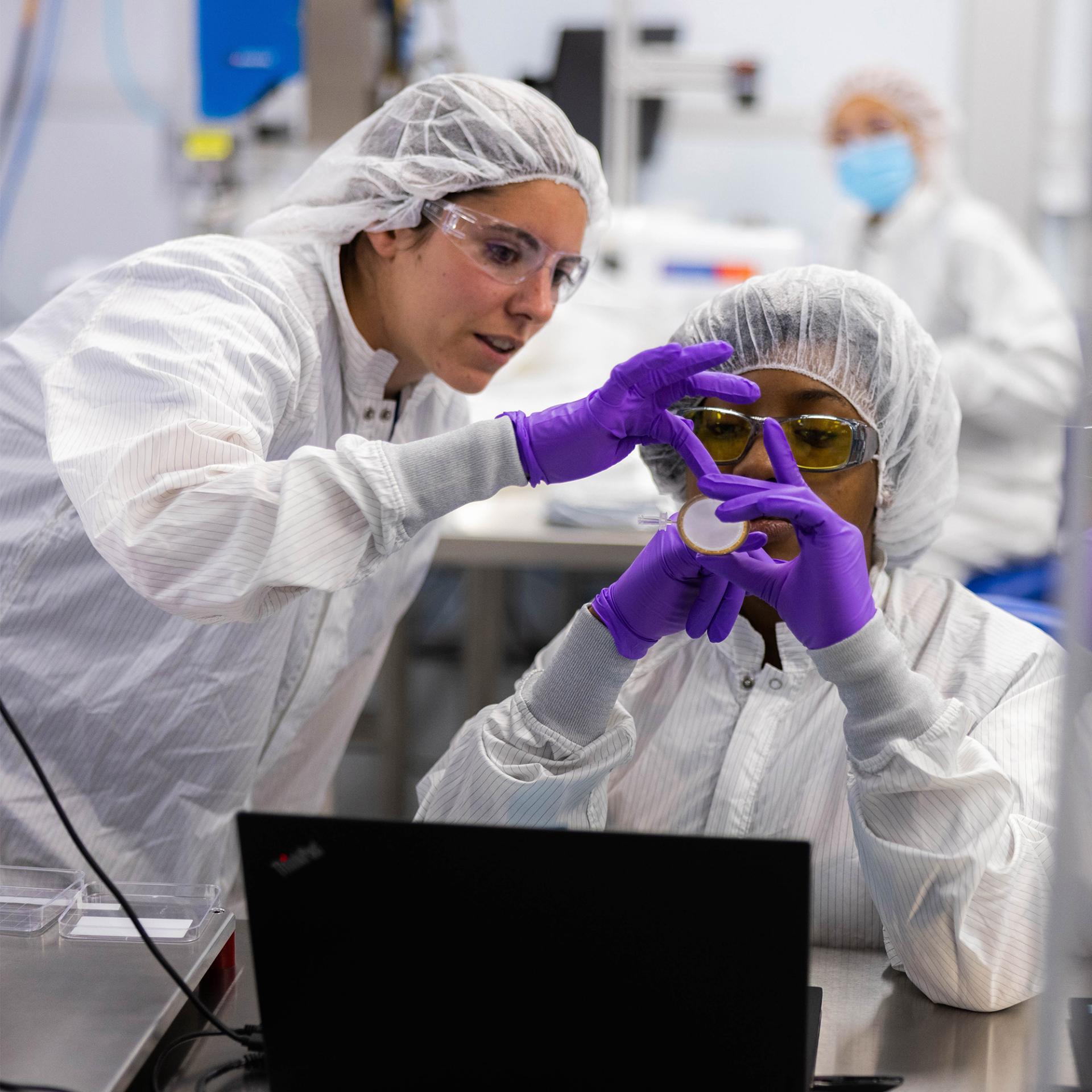 An image of two Vertex scientists in lab coats examining an experiment in the lab