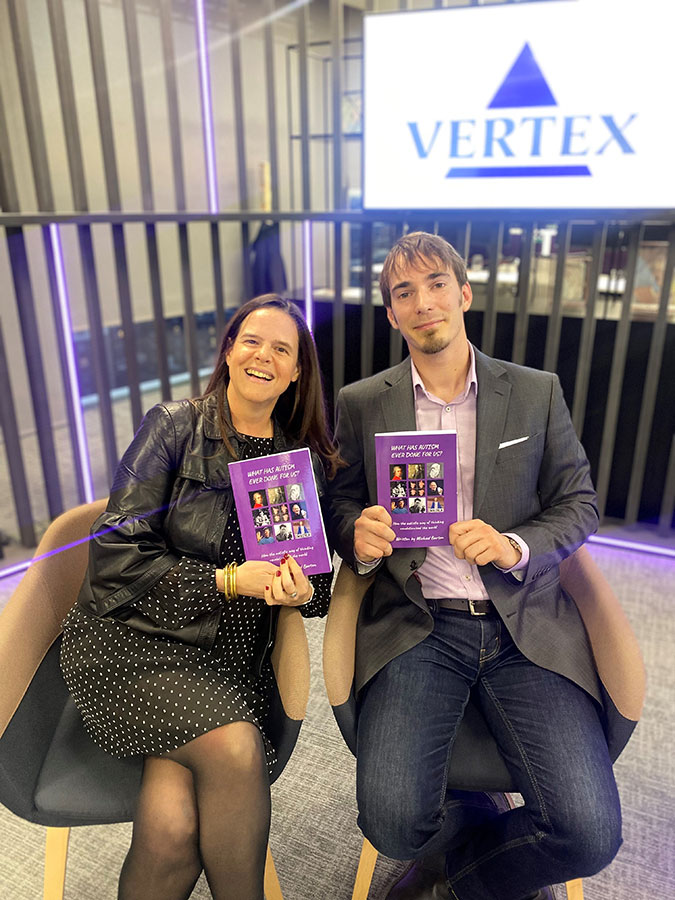 An image of Michael Barton in Vertex's London office holding up his book with a Vertex logo on a screen in the background.