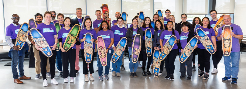 An image of a group of Vertexians wearing purple Day of Service shirts while holding up skateboards they helped design during our 2023 Day of Service.