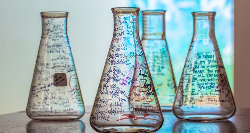 An image of four Vertex Pharmaceuticals culture flasks with messages written on them