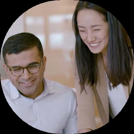 A man sitting down smiling with a smiling female colleague standing next to him