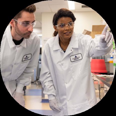 A photo of two Vertex employees in a lab pointing at something