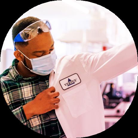 An image of a man putting on a white lab coat that that has the Vertex Pharmaceuticals logo on it.