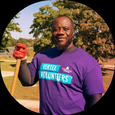 An image of a Vertexian wearing a purple shirt and holding gardening gear while volunteering