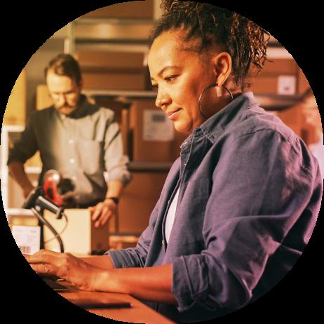 An image of a man and a woman in a room working, she is typing on a keyboard and he is closing a box