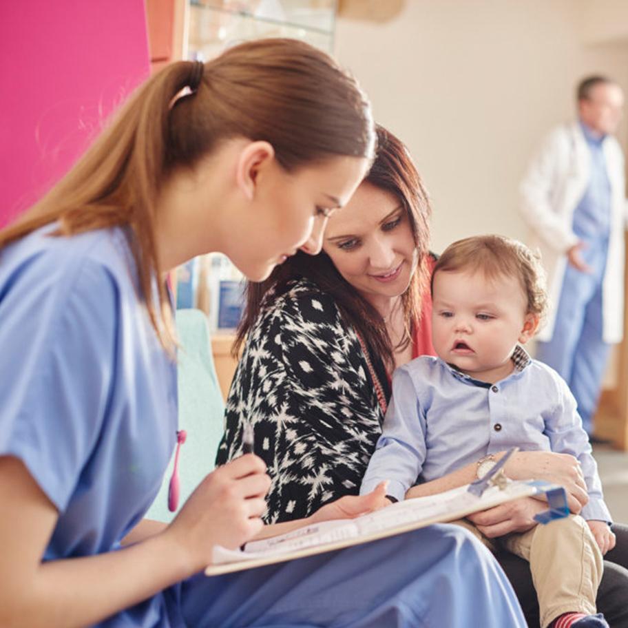 A woman and her small child talk to a medical professional holding a clipboard