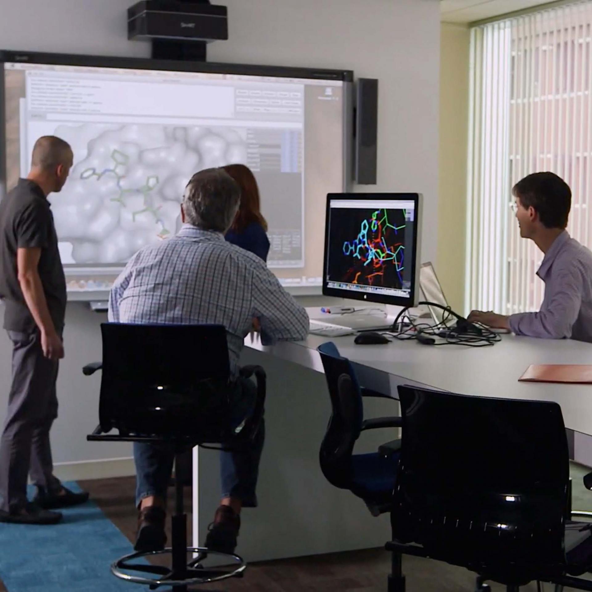 A group of MBA interns sitting in a room reviewing a presentation on screen