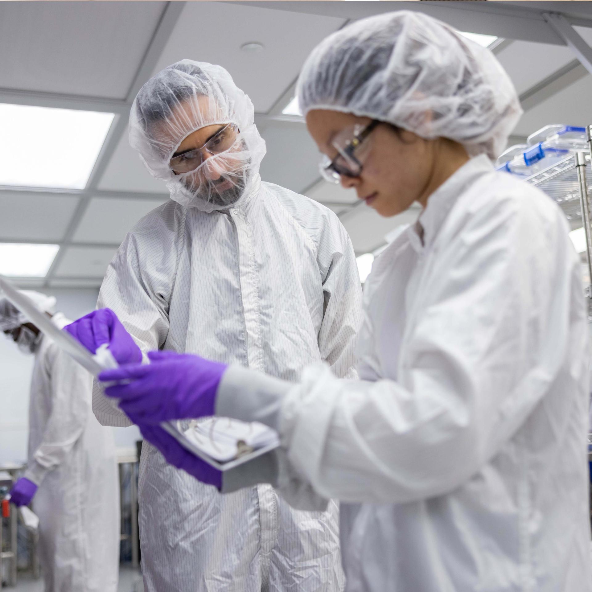 A photo of two Vertex employees in a lab looking at a binder