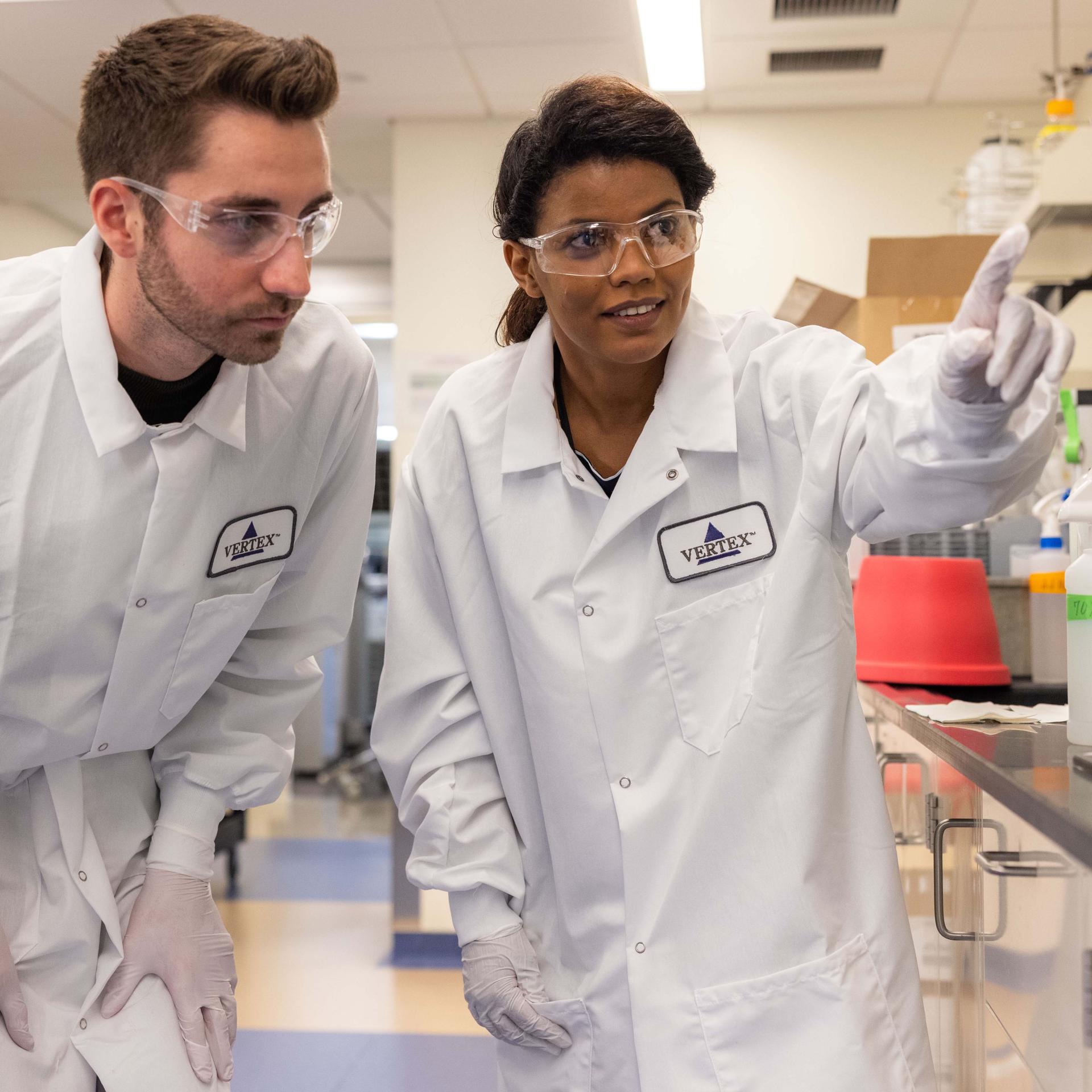 A photo of two Vertex employees in a lab pointing at something