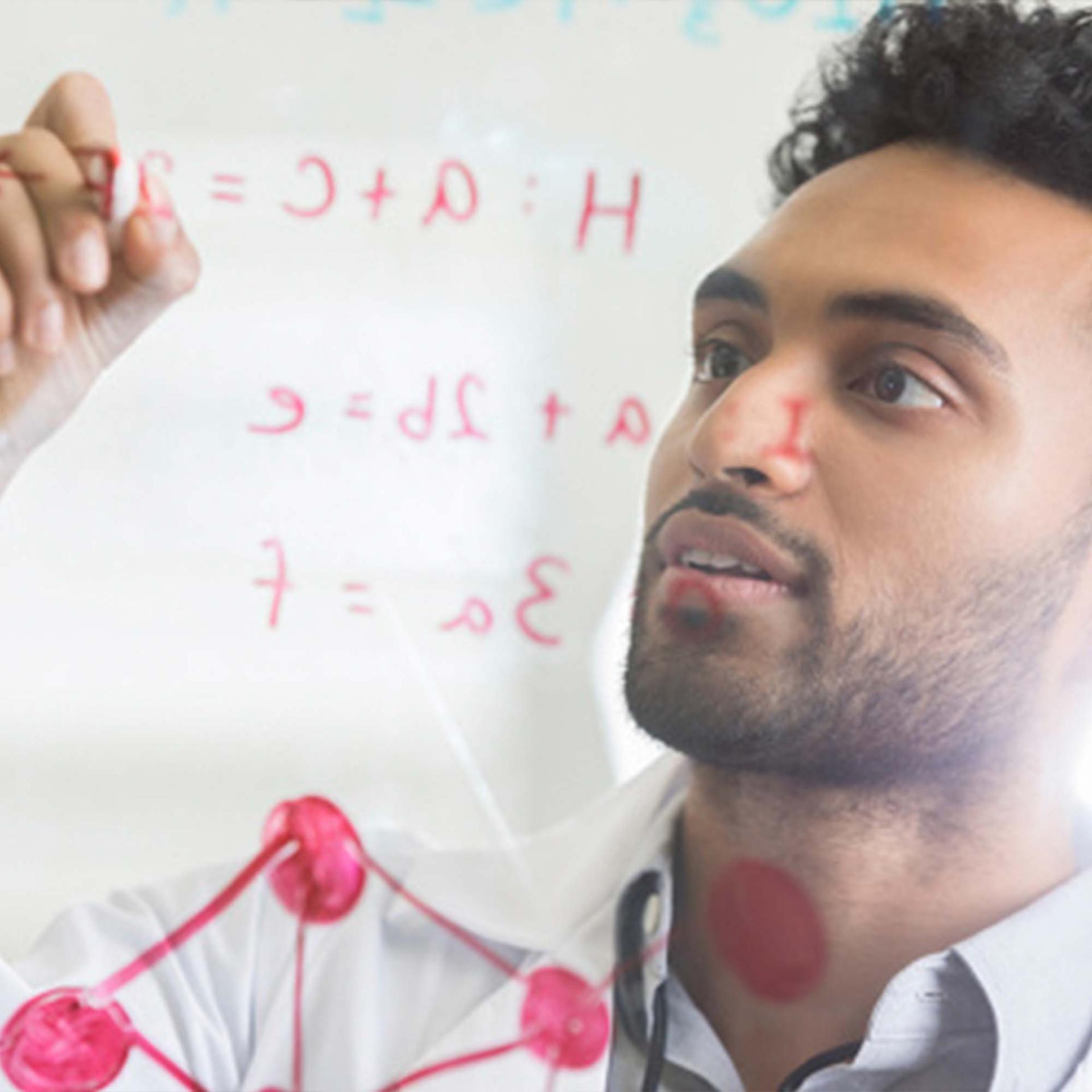 A man writing a formula with a marker on a clear piece of glass