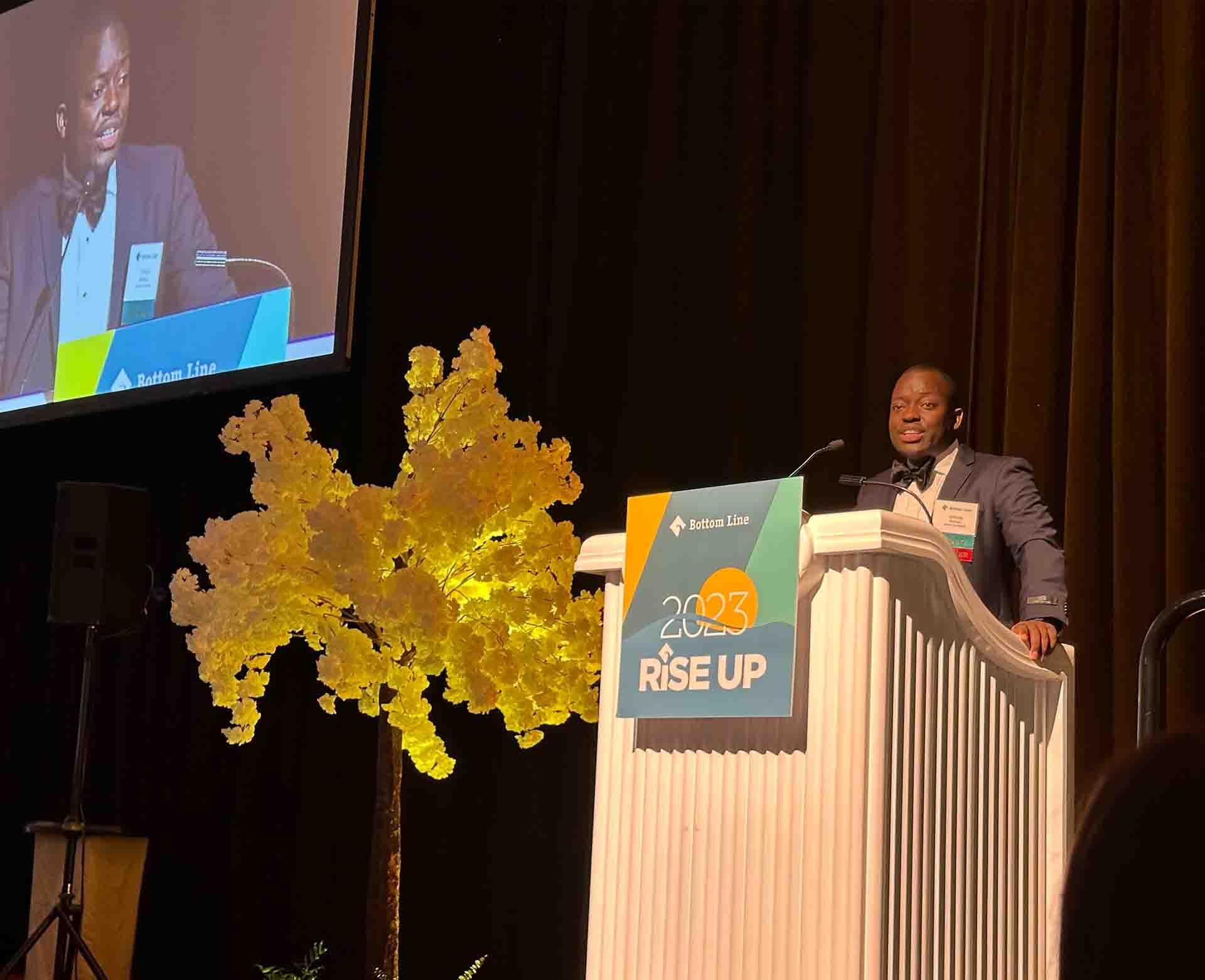 An image of Chiruza Muhimuzi, Vertex Science Leader Scholar and student at the University of Massachusetts, speaking at Bottom Line’s annual Rise Up Gala