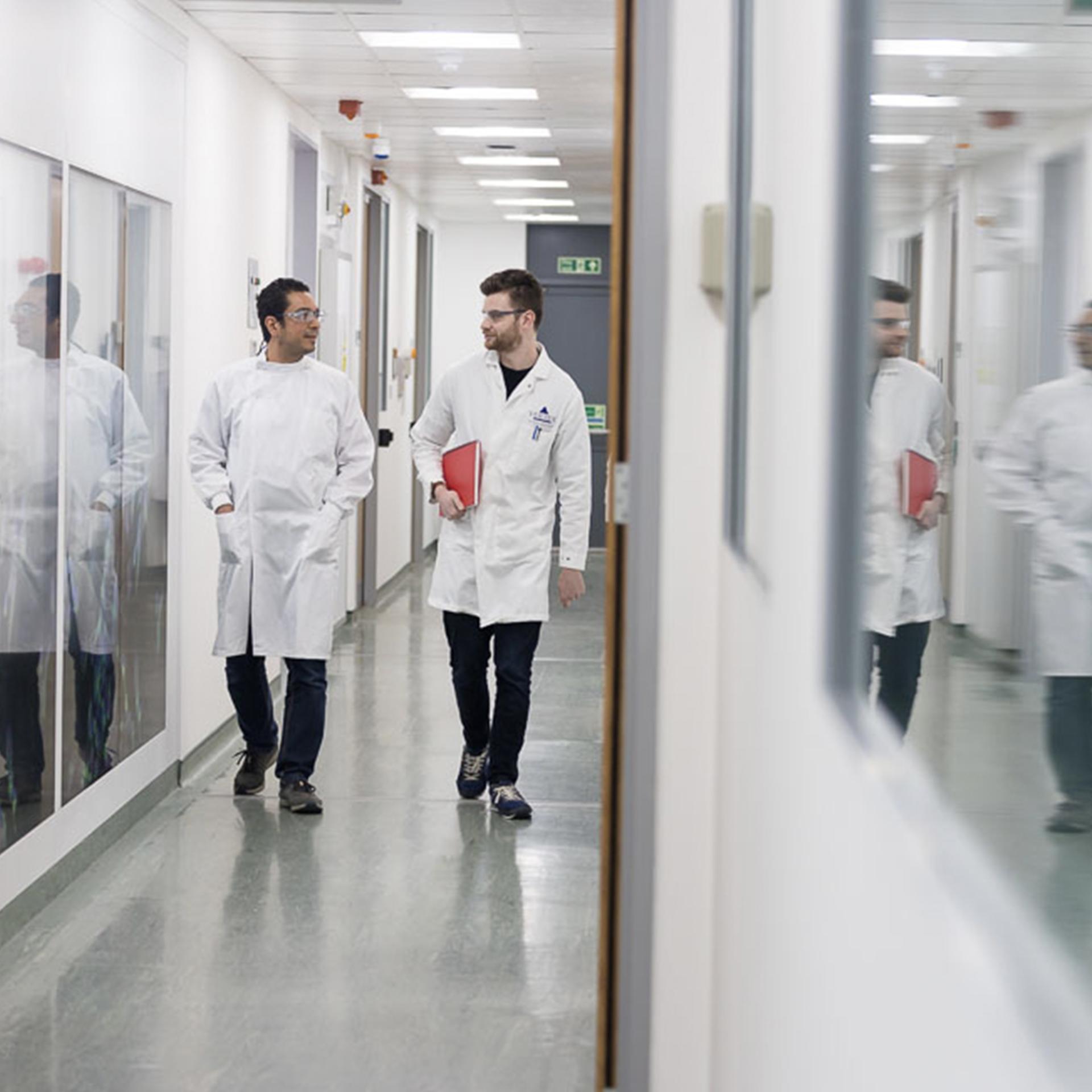 Two Vertex employees in white lab coats walk down a hallway together