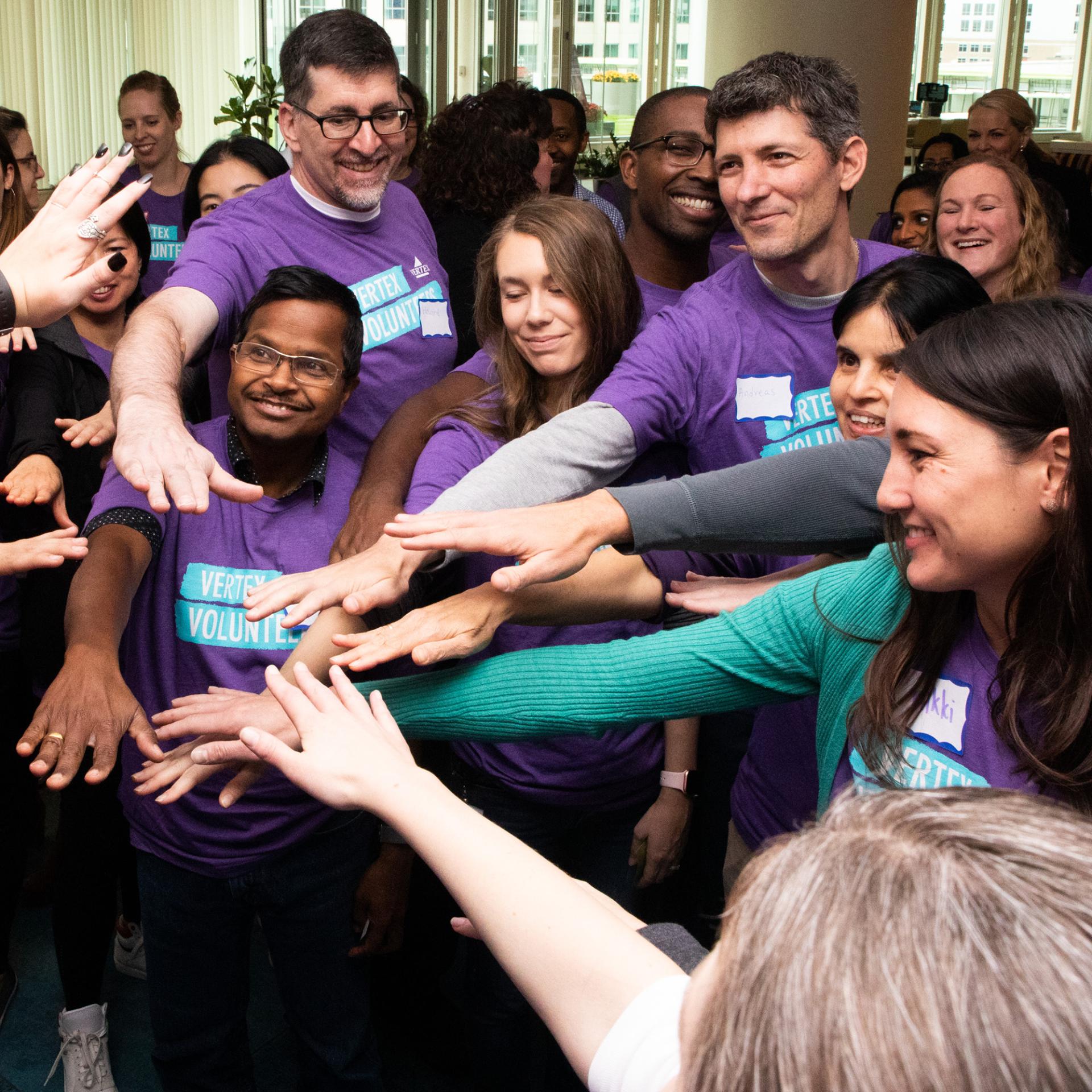 An image of a group of Vertex employees all putting their hands together in a circle