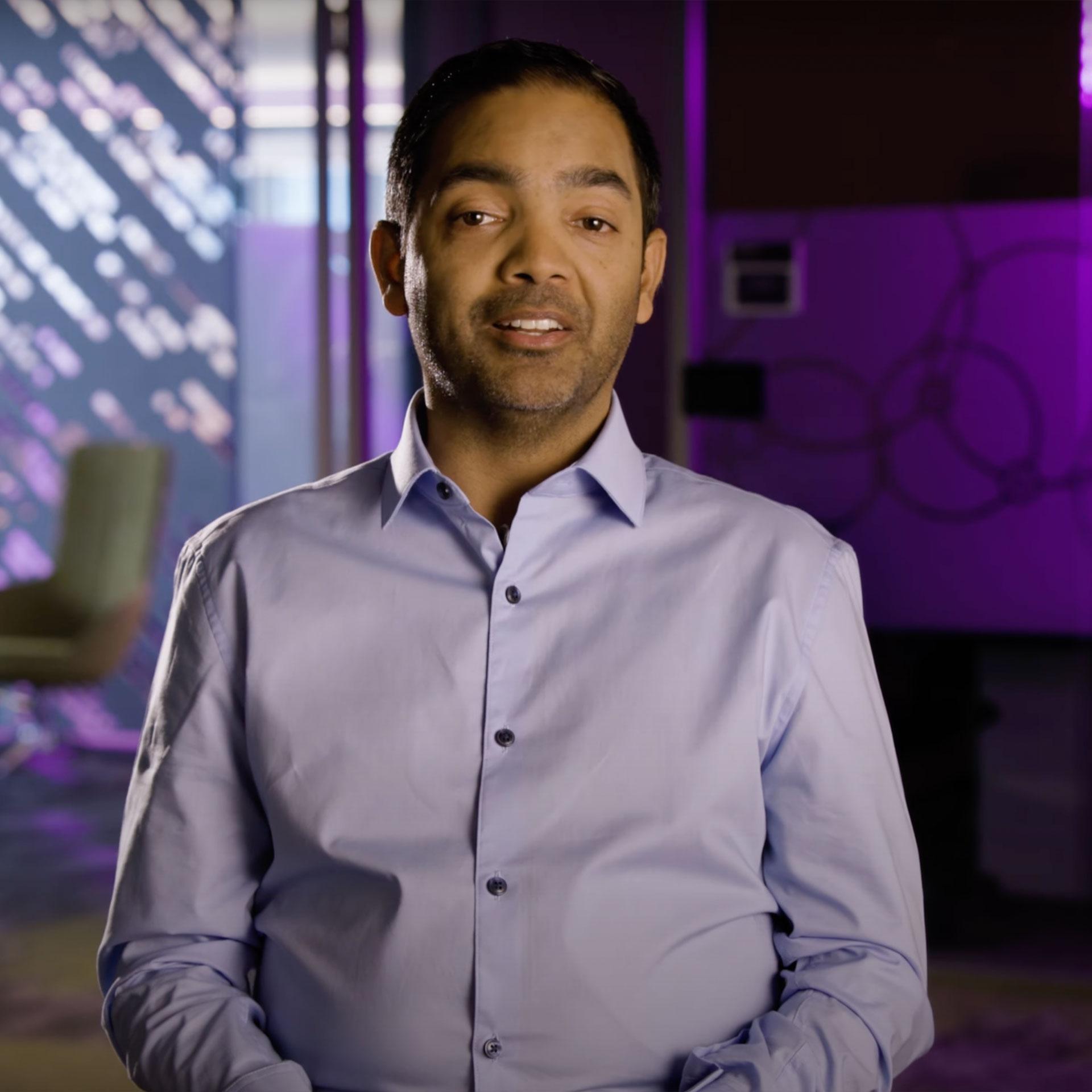 An image of Pranav, a person living with TDT, talking into the camera during an interview. There are purple lights in the background.