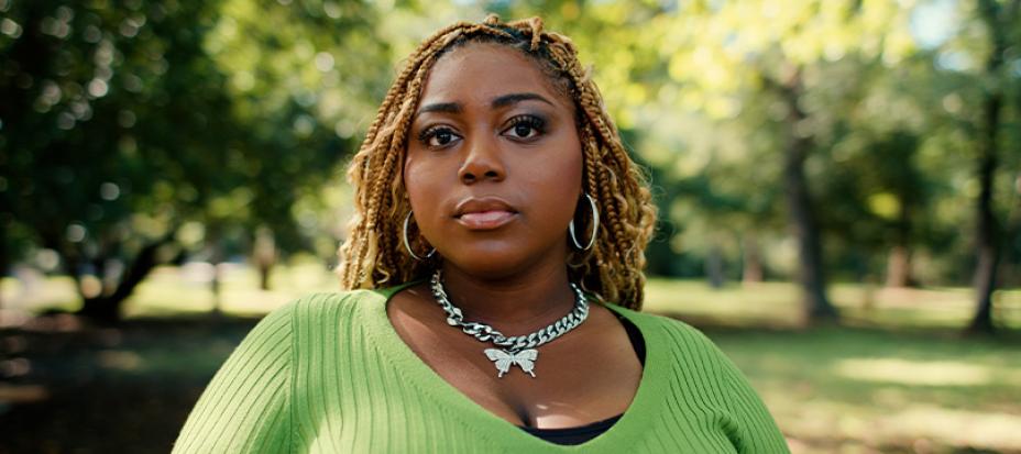 An image of Emani McConnell-Brent standing outside wearing a green shirt and looking at the camera with a serious look
