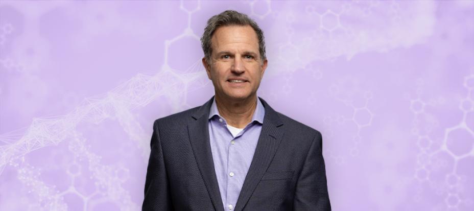 An image of Paul Negulescu smiling while standing in front of a purple background that has faded diagrams of molecules in it