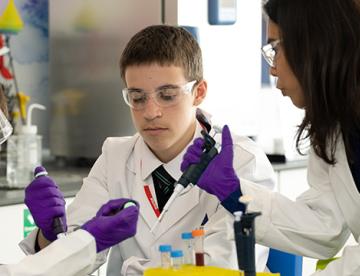 An image of two students in a Vertex Learning Lab being instructed by a Vertex scientist on how to conduct an experiment
