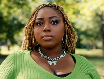 An image of Emani McConnell-Brent standing outside wearing a green shirt and looking at the camera with a serious look