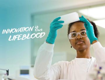 An image of a scientist holding up a tray that reads "Innovation is our lifeblood"