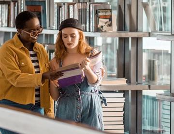 An image of two people in a library looking at a book together