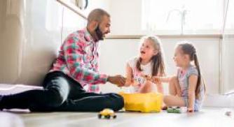 An image of a father and two daughters sitting on the floor playing with toys