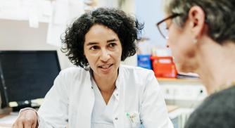 An image of a doctor in a white coat reviewing information on a tablet with a woman